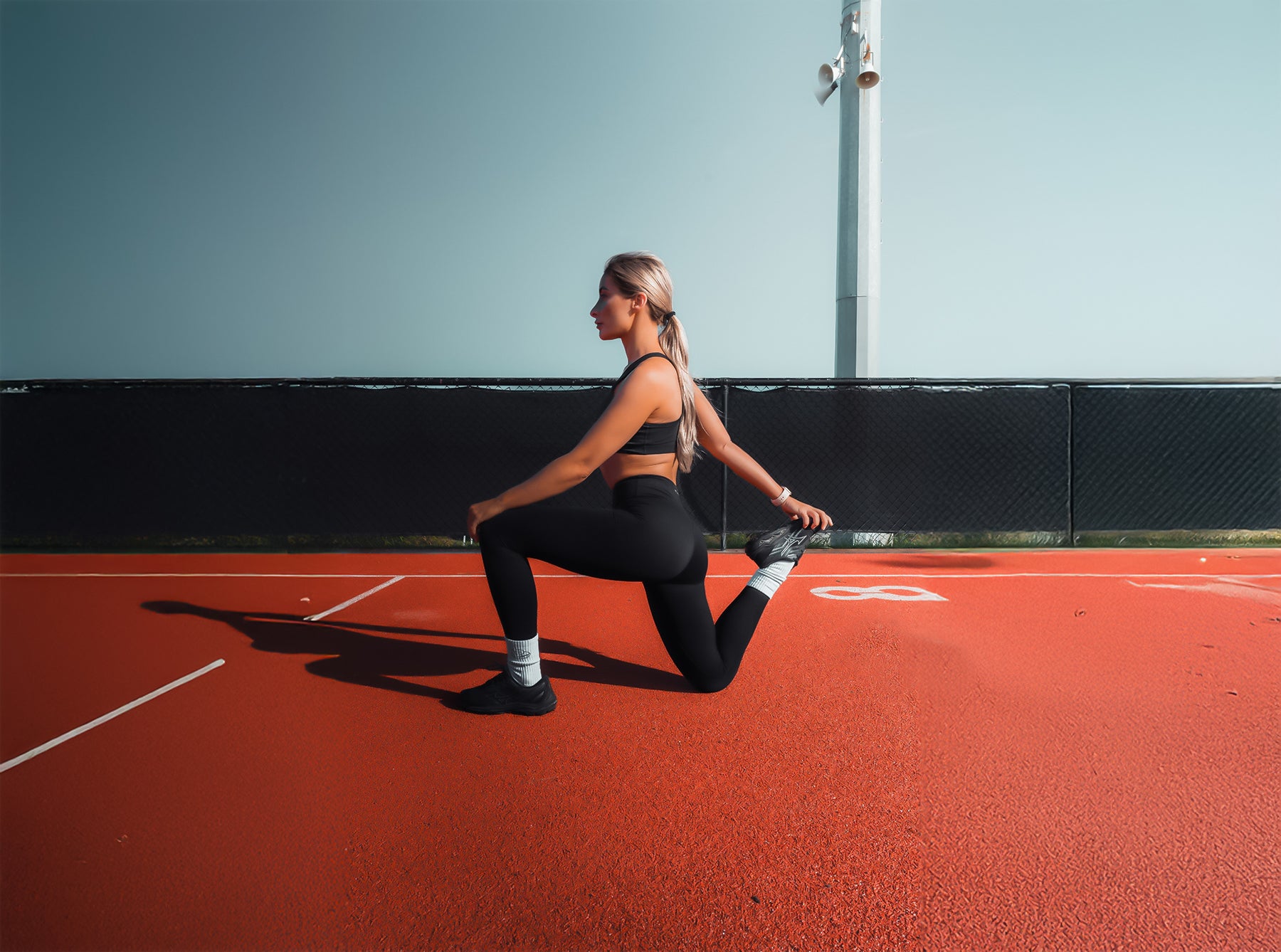 Woman stretching on a red tennis court with a blue wall in the background
